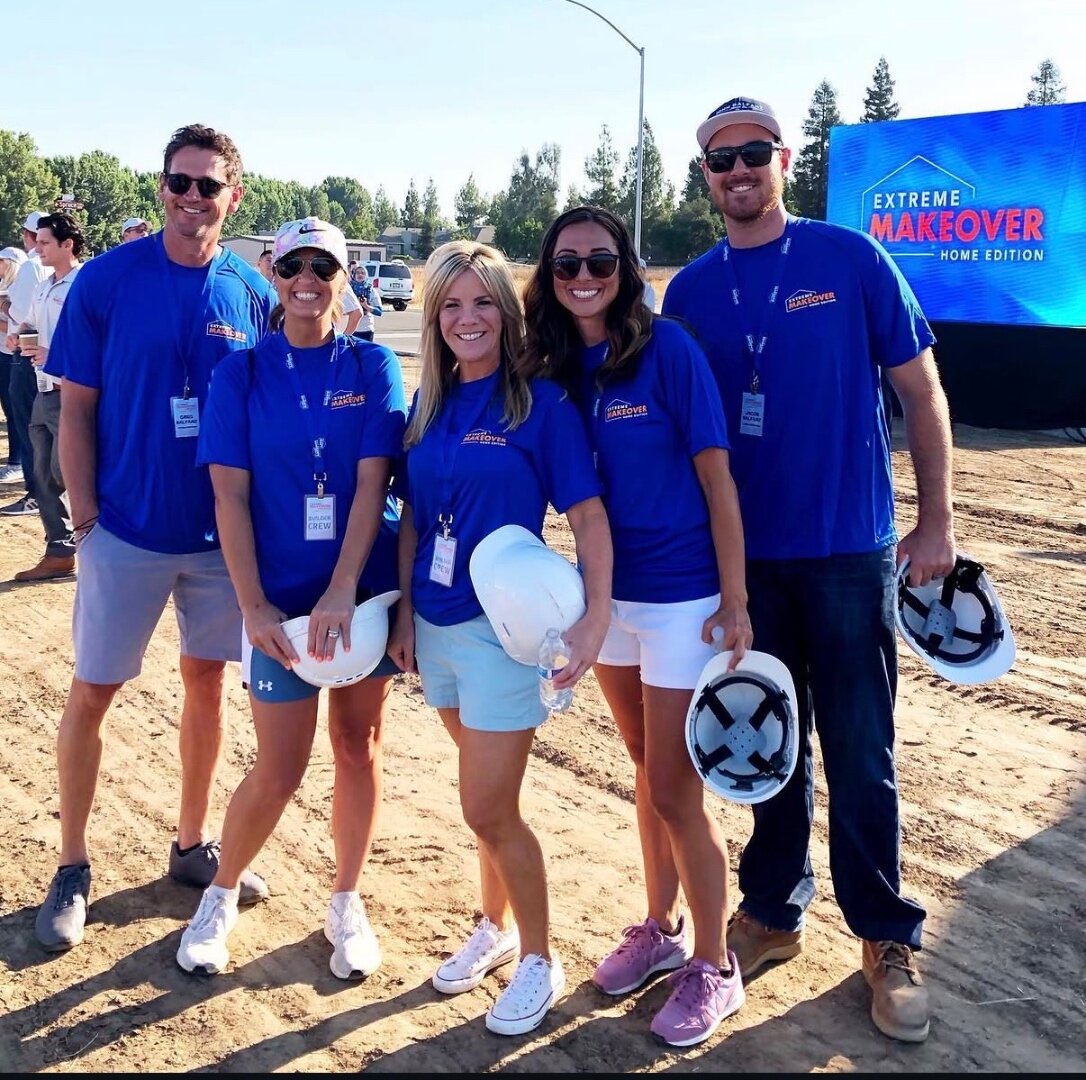 Kelly with the Extreme Makeover: Home Edition build crew in blue shirts holding hard hats in front of the show’s screen