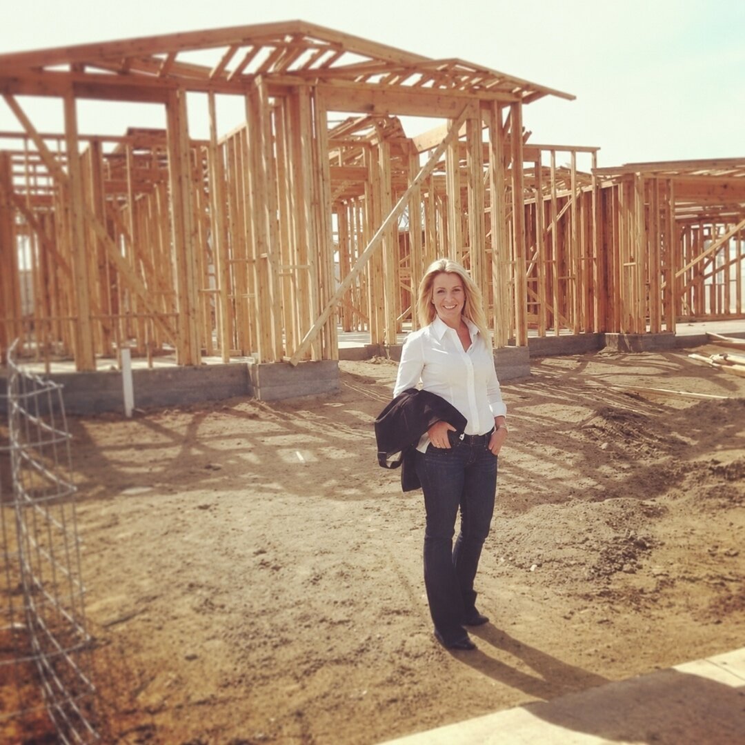 Kelly Allison standing in front of a wood-framed home under construction in Bakersfield, in a white shirt and jeans